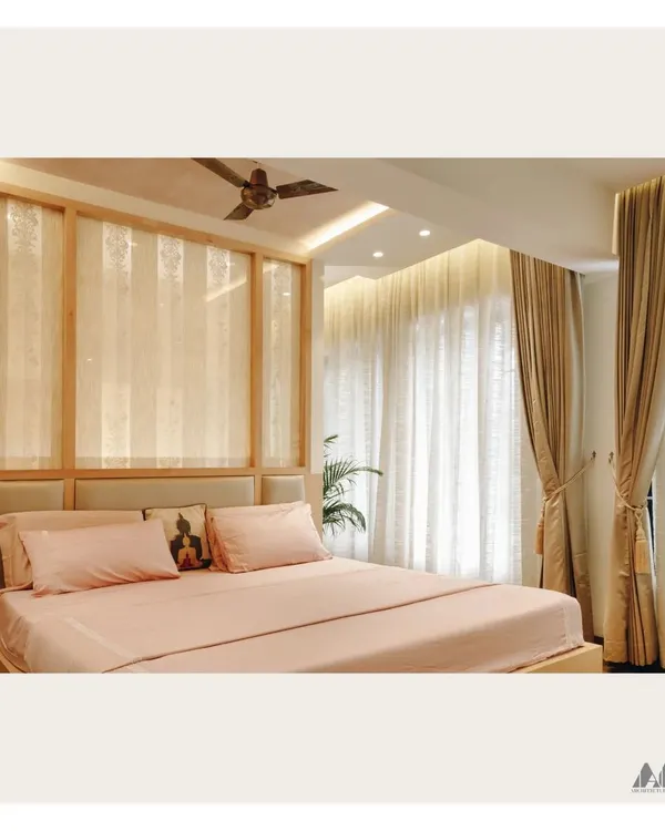 This bedroom is designed for calm and comfort. The space features a custom wooden headboard with translucent panels, soft drapery to filter natural light, and a soothing color scheme.