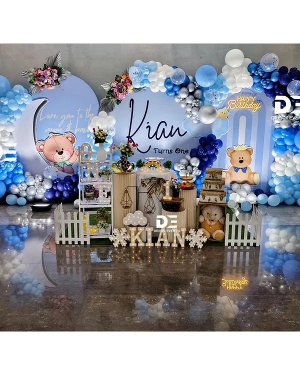 A dreamy 'Love you to the moon and back' teddy bear theme for Kian's first birthday. This elaborate setup features two circular backdrops, a beautiful blue and silver balloon garland, and adorable teddy bear cutouts.
