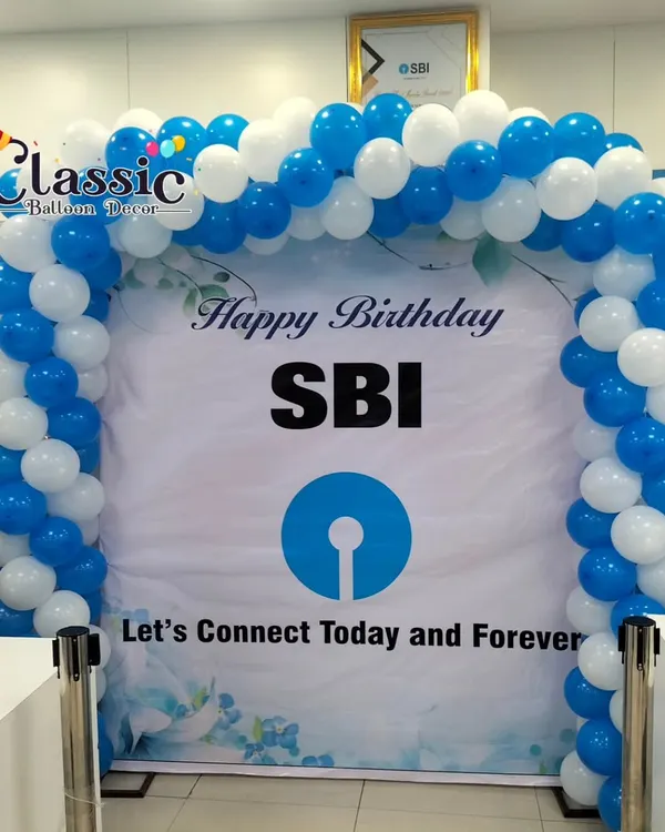 A branded "Happy Birthday SBI" backdrop framed by a blue and white balloon arch inside a bank branch. This setup is ideal for celebrating corporate anniversaries and milestones right where your customers are.