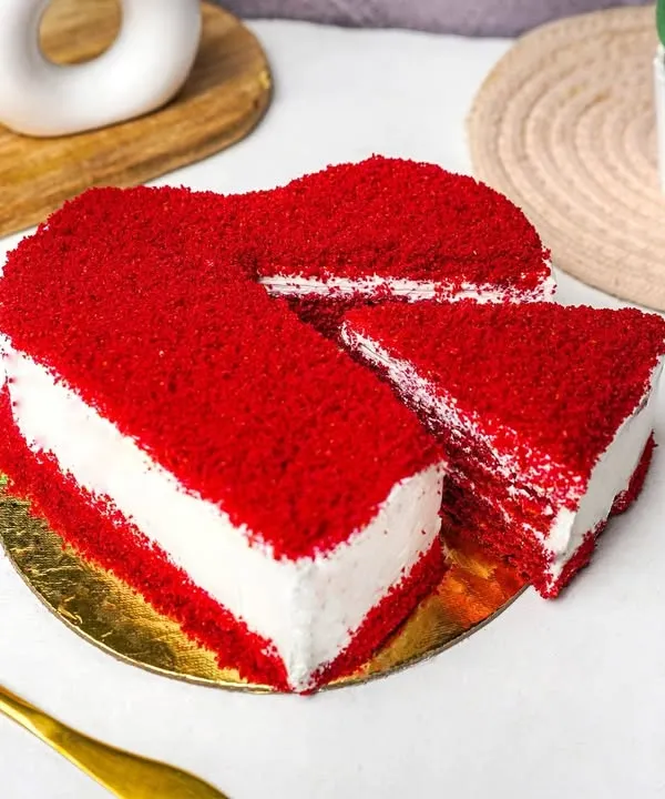 A vibrant heart-shaped red velvet cake with a slice cut out, shot on a clean, bright background.