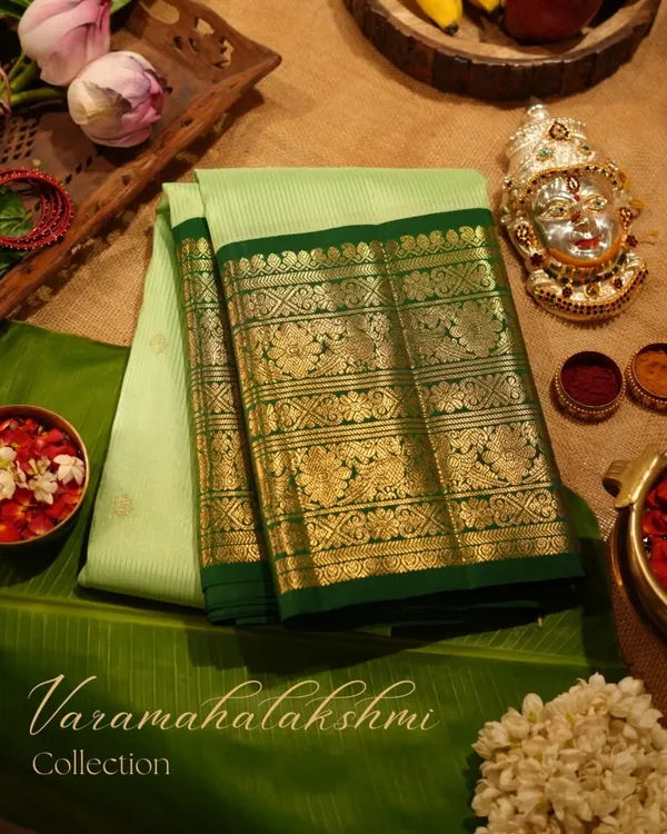 A perfect offering for Varamahalakshmi, this light green Kanjivaram with a dark green peacock border is laid out with traditional puja items.