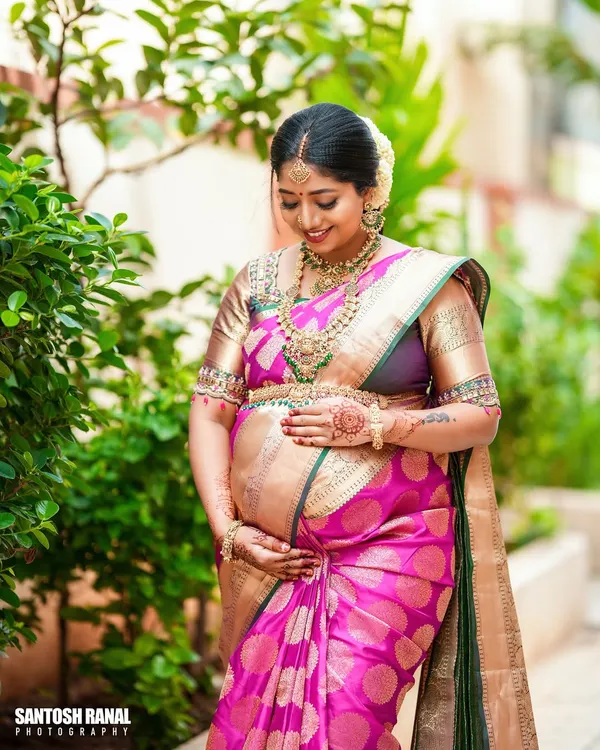 A beautiful outdoor portrait of the mother-to-be on her baby shower day. Dressed in a stunning pink and gold silk saree, she radiates joy and anticipation.