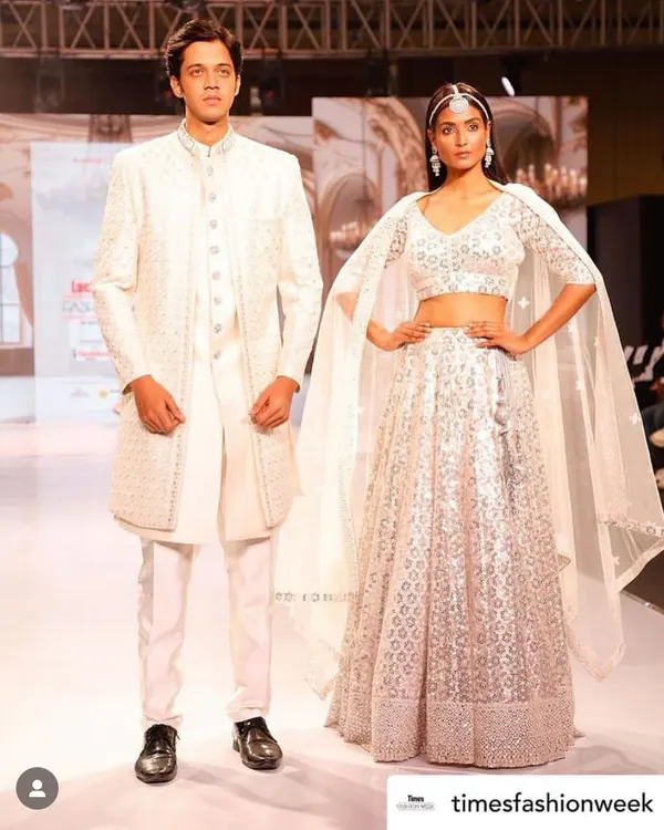 A stunning couple on the runway showcasing our coordinated white collection. The groom's sherwani and bride's lehenga feature matching embroidery, creating a look of pure elegance.