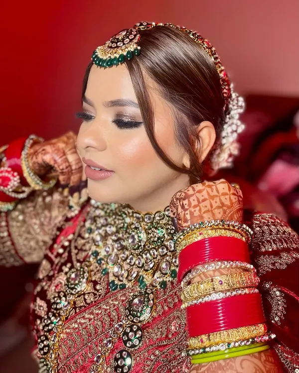 A close-up of this royal bridal look. I created sharply defined, smokey eyes with a touch of glitter and a soft nude lip to perfectly balance the richness of her red velvet lehenga and green jewellery.