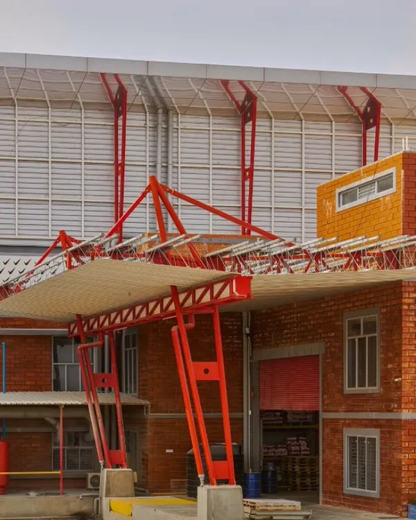 The loading bay of the Varna Paint Factory in Dobbespet, completed in 2017. This image highlights our approach to industrial architecture, where functionality is expressed through bold design. The prominent red structural steel frame contrasts with the exposed brickwork, creating a strong visual identity for a heavy-duty workspace.