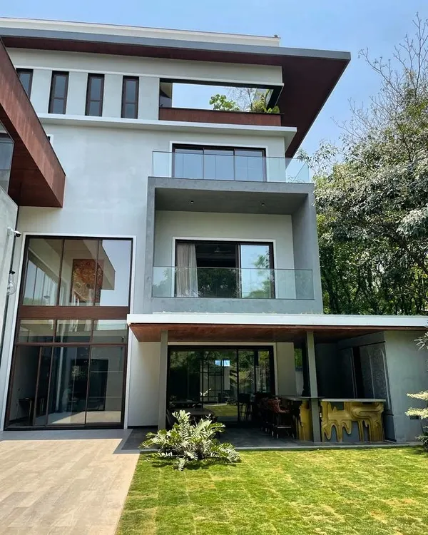 The design for this Koramangala residence features expansive glass, multiple balconies, and a seamless connection to the outdoor lawn and bar area, perfect for modern living.