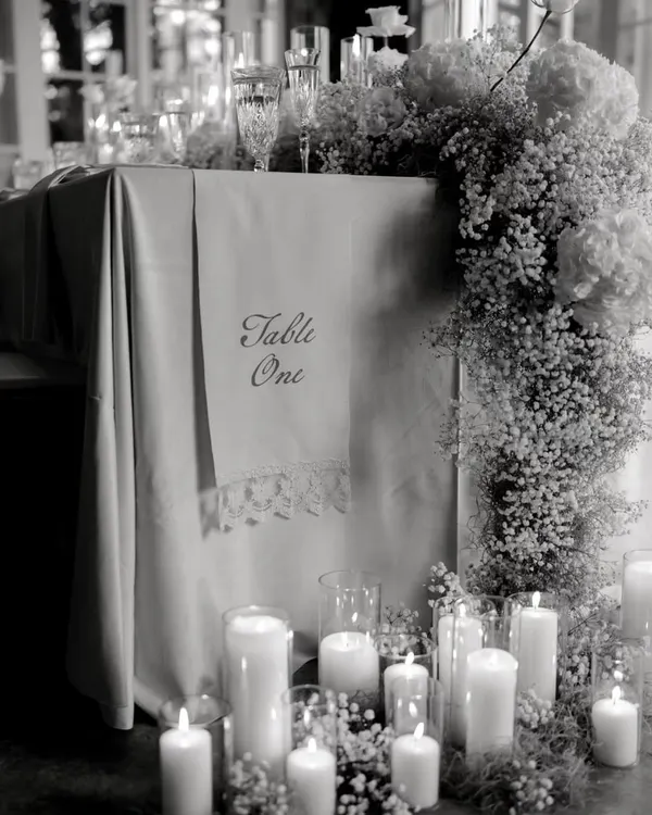 My basics are clear, no basic please. This black and white shot highlights the clean lines and sophisticated details of an all-white tablescape, featuring a cascade of baby's breath and an abundance of candles.