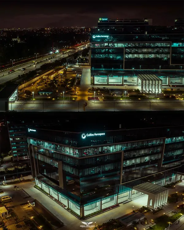 A dramatic night-time aerial shot of the Collins Aerospace building in Bengaluru. Our low-light drone photography highlights the building's modern design and illumination against the city skyline.