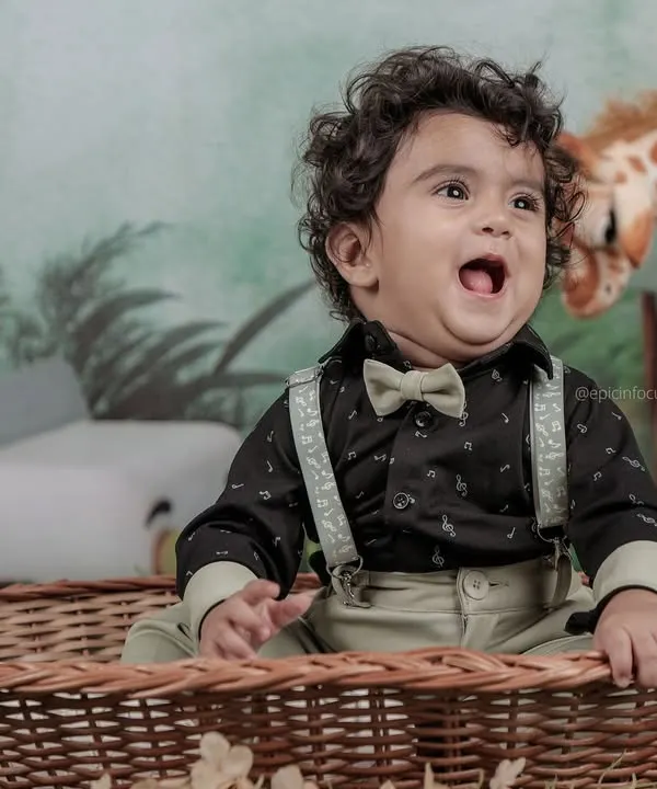 This little explorer, dressed in a bow tie and suspenders, looks up with excitement in our jungle-themed setup, complete with a friendly giraffe prop.