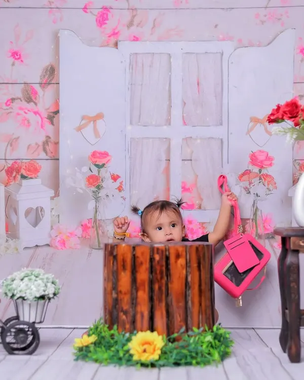 A peek-a-boo moment from inside a rustic prop. This playful shot in our floral garden setup adds an element of surprise and fun to the baby girl's photoshoot.
