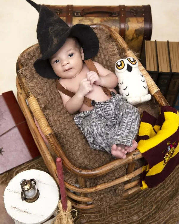 An alternate angle from the Harry Potter themed shoot, this time with the baby awake and looking at the camera. This shot captures the detailed props like the sorting hat, suspenders, and a plush owl.