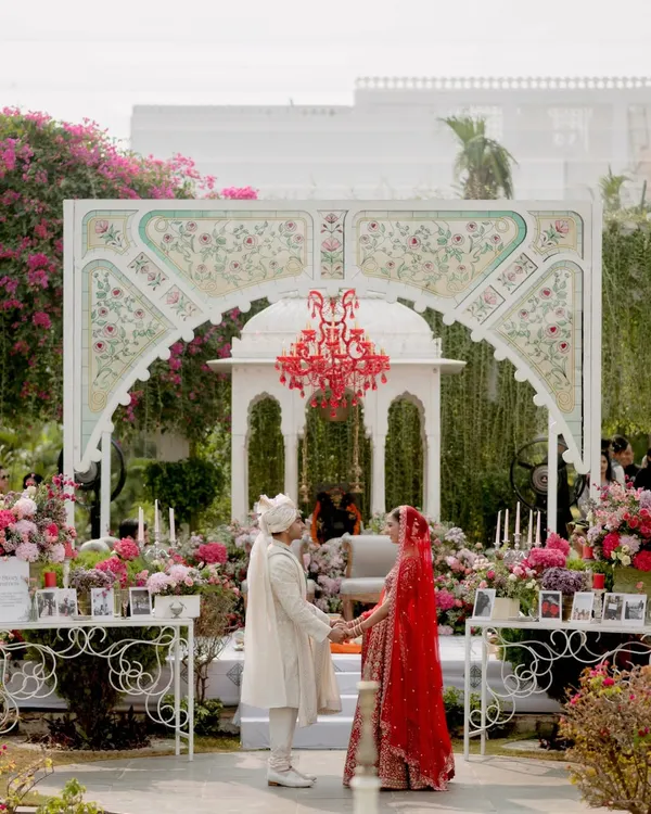 A full view of the hand-painted mandap backdrop we created for Sarah and Vikram's "Tale as Old as Time" wedding. The stunning red chandelier served as the focal point, surrounded by a garden of pink and red florals.