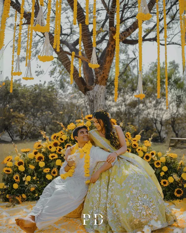 A dreamy Haldi setup under a tree, with hanging marigold garlands and a seating area nestled in a bed of sunflowers. This is how we turn a traditional ceremony into a fairytale moment.