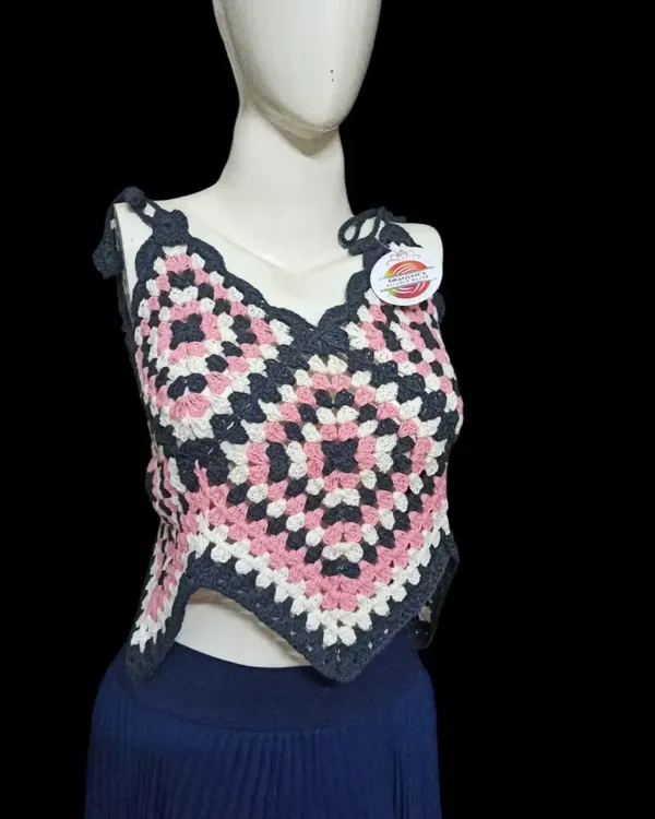 This handkerchief-style top is made from a large granny square, creating a unique pointed hem. The color combination of pink, white, and charcoal grey makes it a modern and eye-catching piece.