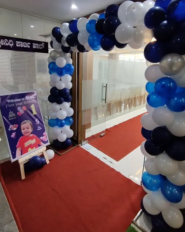 A classic blue, white, and silver balloon arch creating an inviting entrance for a first birthday party. A personalized welcome sign is placed at the entrance.