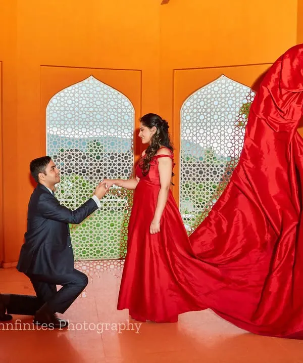 A dramatic proposal scene enhanced by a flowing red gown, captured in our studio. We expertly manage fabric to create dynamic, wind-swept effects for a high-fashion look.