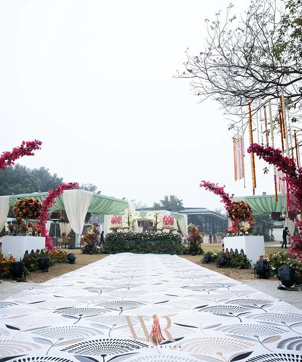 The entrance to a bohemian dream. I used a printed carpet to create a unique aisle, leading to arches adorned with vibrant pink bougainvillea, creating a joyful and spirited welcome for this day wedding.