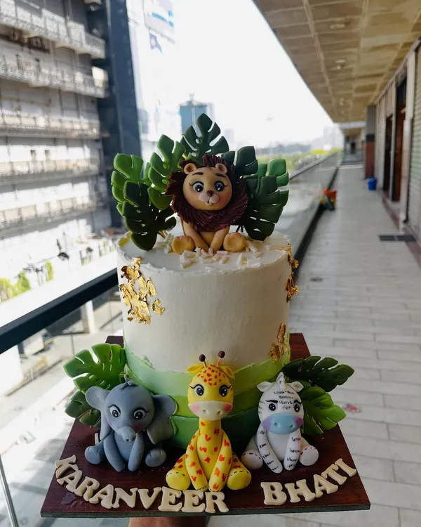 A delightful jungle safari cake featuring a fondant lion, elephant, giraffe, and zebra. The cake is decorated with lush green leaves and touches of gold leaf for a hint of wild elegance.
