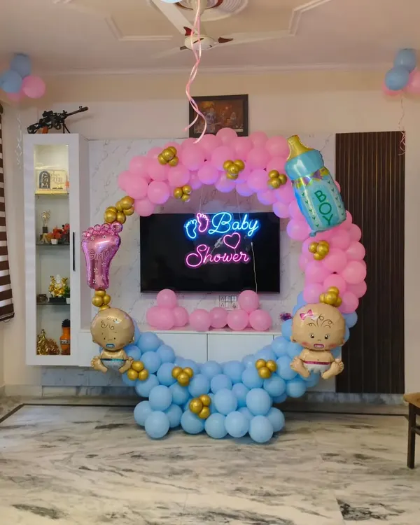 A classic baby shower decoration for a home setting. I created a balloon ring with pink and blue sections, a 'Baby Shower' neon sign, and themed foil balloons like a baby bottle and foot.