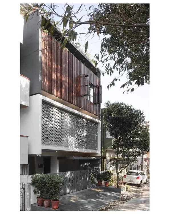 The '10 x 10 Residence' stands on a compact 30x30 feet plot in a dense urban area. The facade is a study in contrasts, with a solid, textured 'jaali' screen on the first floor and a lighter, slatted wooden screen on the second.