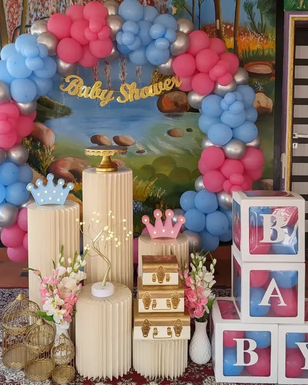 A fun and modern baby shower decor for a gender reveal party. The setup includes a pink and blue balloon arch, "BABY" blocks, and decorative pedestals with props.