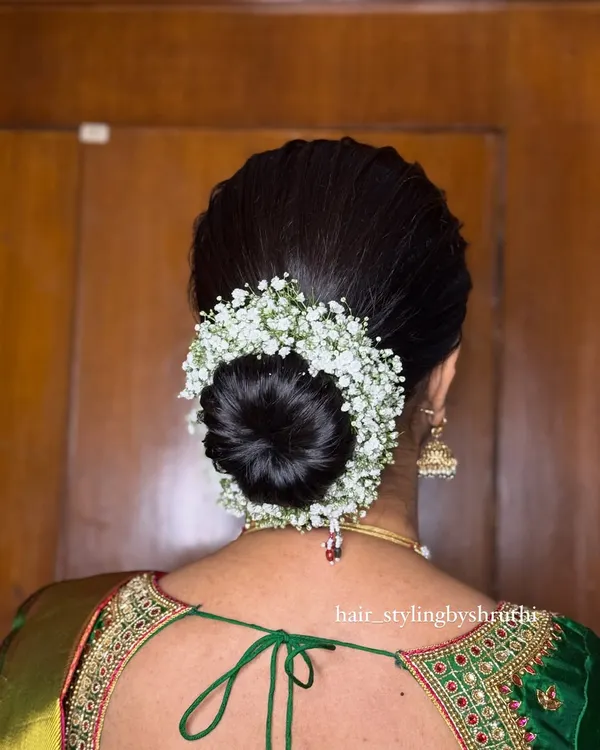 A classic, neat bridal bun completely encircled with a gajra of fresh baby's breath. This is a timeless and elegant updo that pairs perfectly with a traditional silk saree for any wedding function.