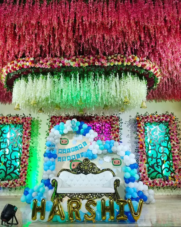 A spectacular stage we created for a 'Welcome Baby' ceremony. The centerpiece is an elegant white sofa, set against a backdrop of blue and white balloons, custom banners, and the baby's name in large gold foil letters.