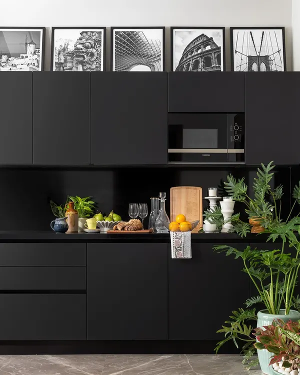 A sleek and moody all-black kitchenette in the Juneja Residence. The minimalist, handle-less cabinets create a seamless look, while the black-and-white architectural photographs above add a personal and artistic touch.