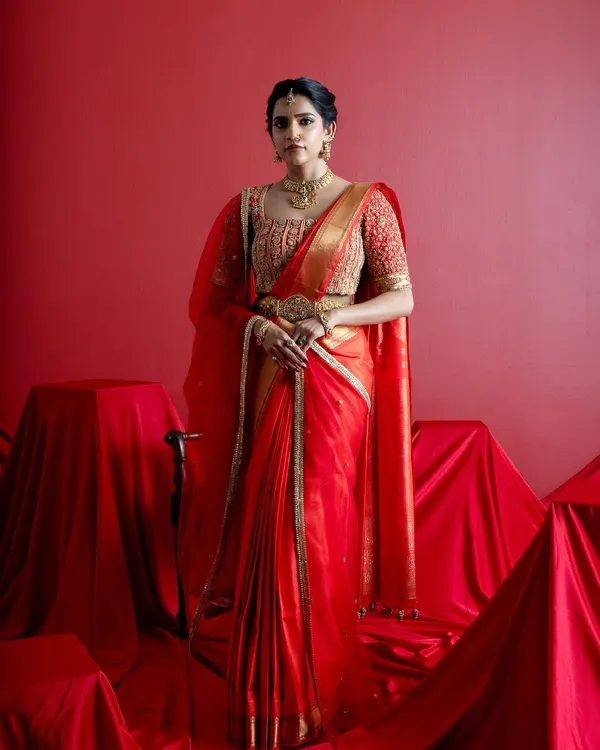 A full-length portrait of a bride in a classic red and gold Kanjeevaram saree. Paired with a heavily embroidered custom blouse and traditional temple jewelry, this look embodies the grace and grandeur of a South Indian wedding ceremony.