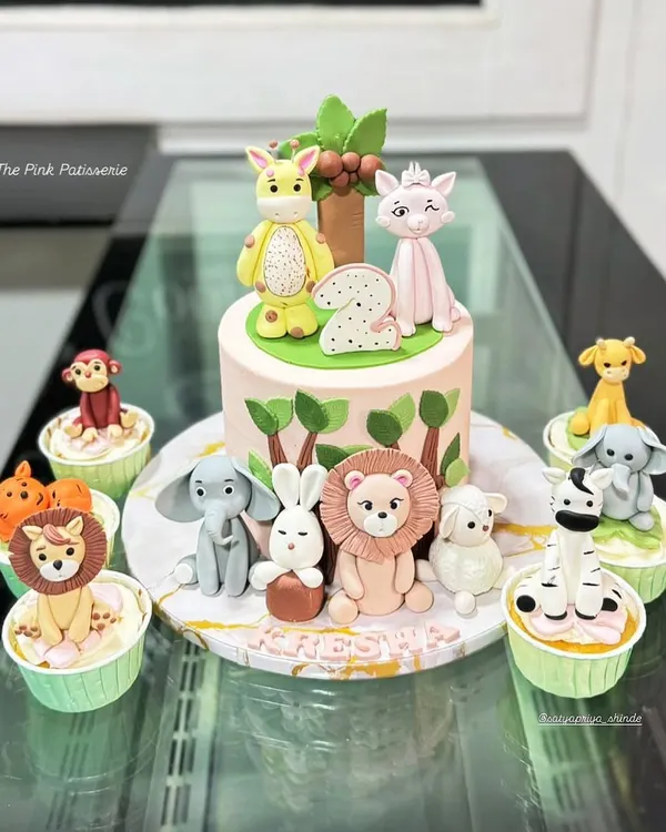 This jungle-themed cake, complete with handcrafted fondant animals and matching cupcakes, is perfect for a memorable first birthday party. We designed this entire set to create a stunning dessert table centerpiece.