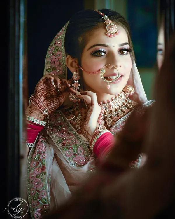 A beautiful getting-ready shot of the bride looking into a mirror. This candid moment captures her adjusting her earring, with a soft smile that reflects her excitement for the day ahead.