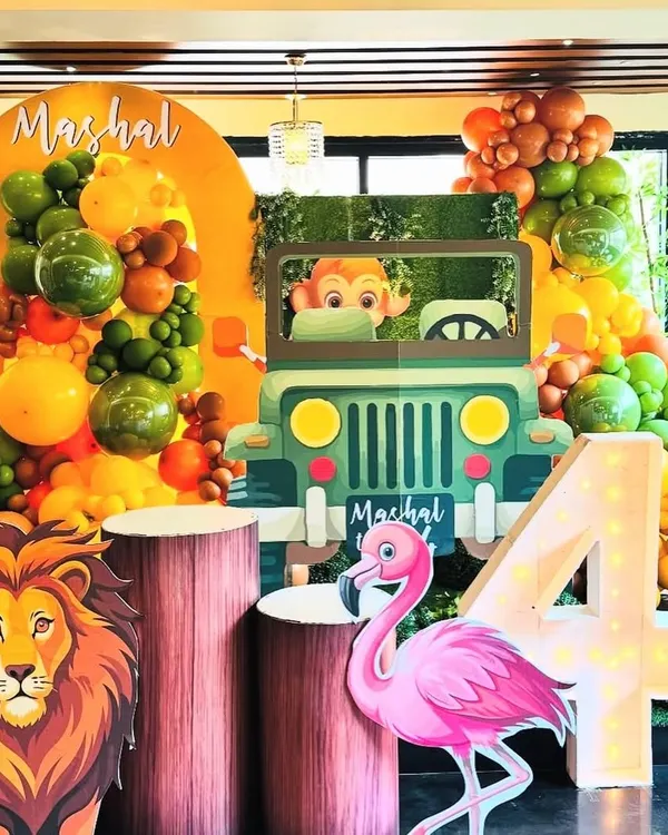 A full view of our jungle safari decor, showcasing the large light-up number '4', a friendly flamingo, and a mighty lion standing guard. The setup is brought to life with a custom jeep photo booth and a backdrop personalized with the birthday boy's name, Mashal.