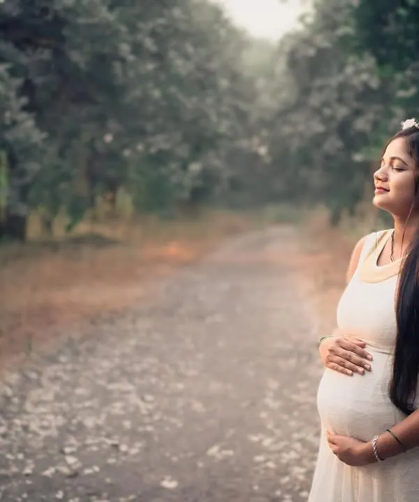 A serene solo portrait of a mother-to-be enjoying a quiet moment on a peaceful forest path. The natural light filtering through the trees creates a soft and gentle atmosphere.