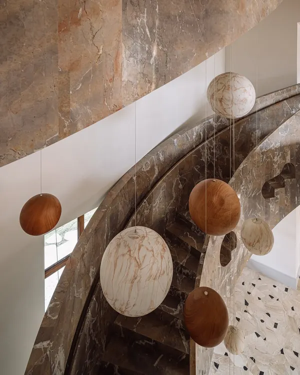 The sculptural staircase at Rehethaan is a celebration of form and material. Clad in dramatic brown marble, it curves its way up, with a celestial installation of spheres hanging in the void.
