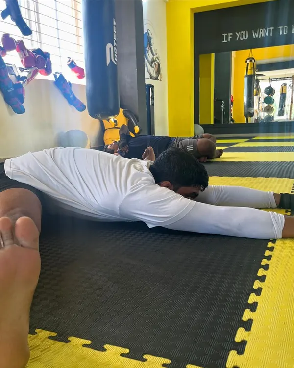 A member performs a deep pancake stretch on the mats, an essential cool-down for improving hip mobility and flexibility.