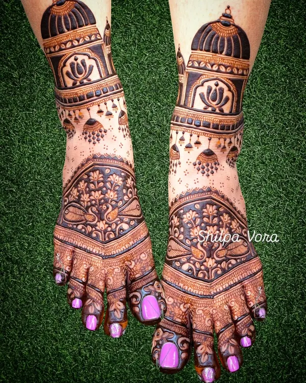 A stunningly detailed bridal foot design, featuring architectural domes, hanging 'jhumka' earrings, and delicate peacock motifs.