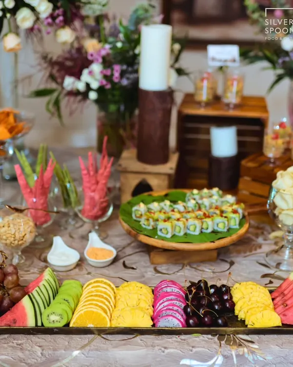 A lavish spread featuring a variety of global and local favorites. The table includes a platter of fresh sushi, an assortment of colorful cut fruits, and other appetizers, perfect for a birthday celebration.