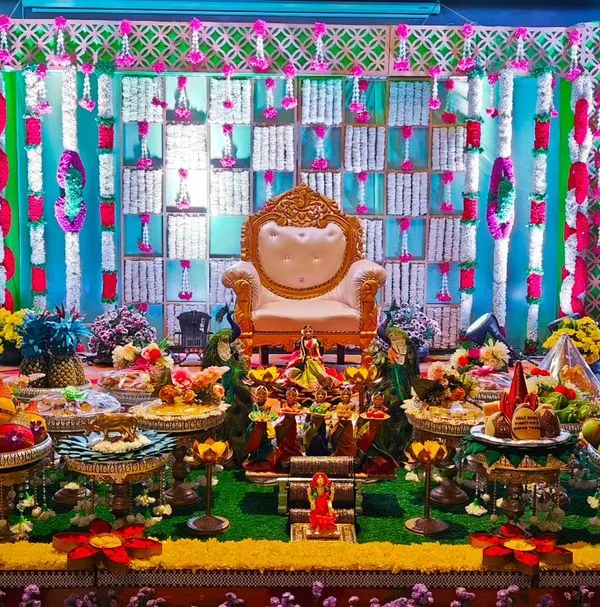 A symphony of culture and grace for a puberty function. The stage is adorned with hanging floral garlands, large decorative pots, and a full display of traditional offering plates.
