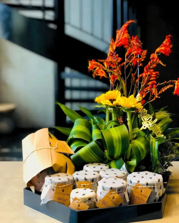 This custom hamper is a great example of my collaborative process. It combines jars of homemade preserves and a beautifully wrapped cake with a vibrant floral arrangement, all nestled in a sleek tray for a client's special occasion.