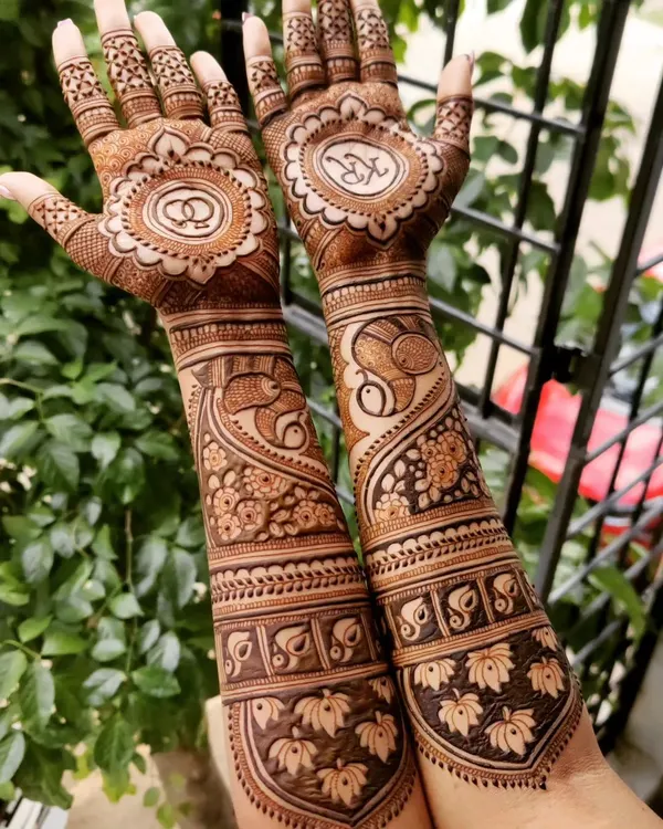 This engagement mehendi was designed to tell a story, with the couple's initials and wedding rings in mandalas on the palm. The arms feature elegant peacock and swan motifs, symbolizing love and partnership.