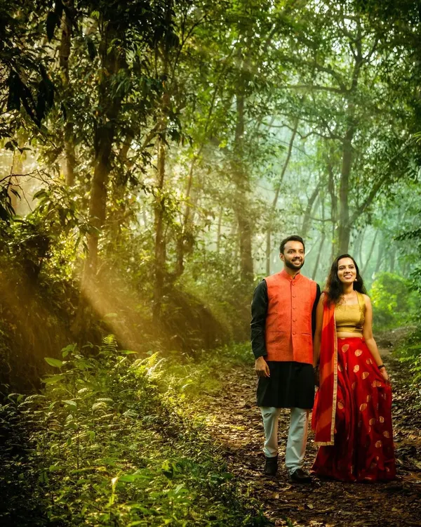 A couple walks through a forest path as beautiful sunbeams filter through the trees. This golden hour photography creates a magical and romantic atmosphere, perfect for an outdoor pre-wedding shoot.