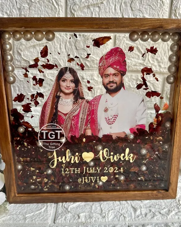 This 10-inch square teakwood frame is filled with resin, preserving the couple's varmala petals. Their photo is centered, with names, date, and hashtag in gold.