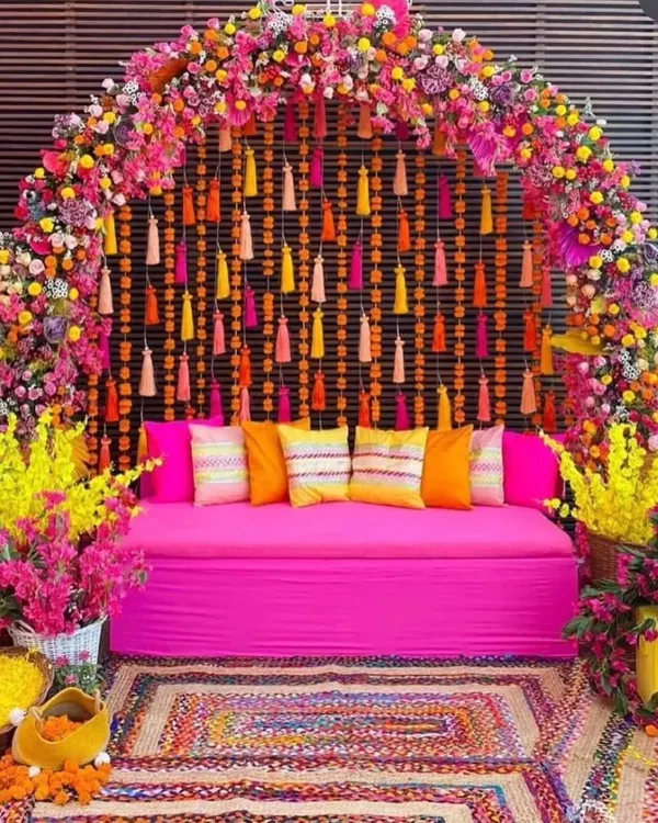 I create vibrant, picture-perfect backdrops for your Mehandi or Haldi ceremony. This setup features a comfortable pink diwan, a floral arch bursting with color, and traditional tassel hangings that make for amazing photos.