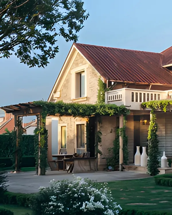 A blend of sloping red roofs, a vine-covered pergola, and soft neutral facades brings this home into harmony with its lush green landscape. It is a statement in contemporary architecture rooted in classic forms.