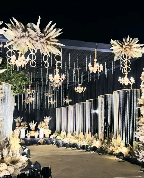 Make a statement with a dramatic nighttime entrance. This design uses illuminated pampas grass arrangements, hanging chandeliers, and crystal curtains to create a luxurious and unforgettable welcome for an exclusive evening gala.