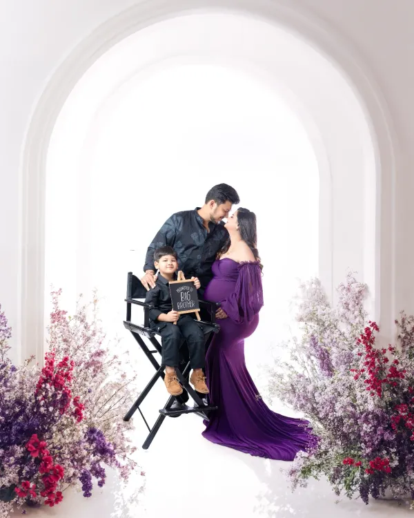 A beautiful family portrait celebrating the upcoming arrival. This sibling maternity session is set against a classic white arch in my studio, framed with delicate flowers to create a dreamy, light-filled atmosphere.