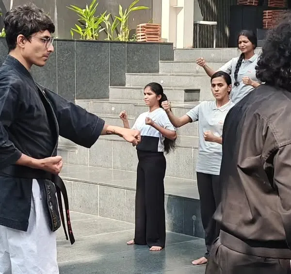 An instructor demonstrates a blocking technique during a self-defense workshop for female students at ISBR Business School in Bengaluru. The focus is on clear, step-by-step instruction.