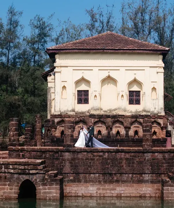 A destination wedding portrait in Goa, using the unique architecture of a historic temple and water tank to create a stunning, wide-angle shot.