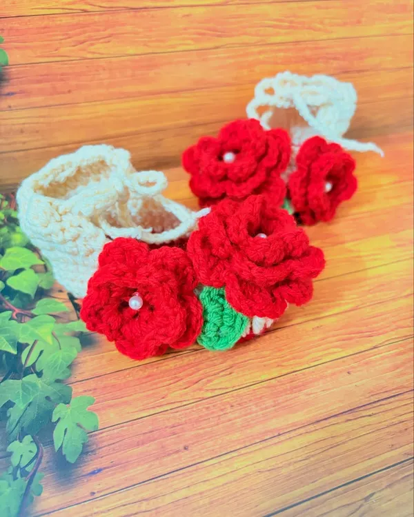 A close-up of my handmade booties with vibrant red flowers. Each flower is centered with a small pearl for a touch of elegance.