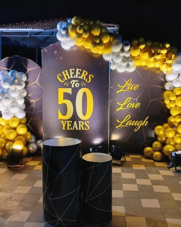 A classy 'Cheers to 50 Years' celebration. This outdoor setup uses a sophisticated black and gold theme with elegant backdrops, a balloon arch, and uplighting for a dramatic effect.